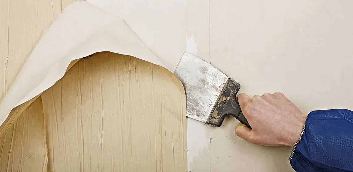 Handyman removing wallpaper with a scraper for wall preparation in Minneapolis, MN