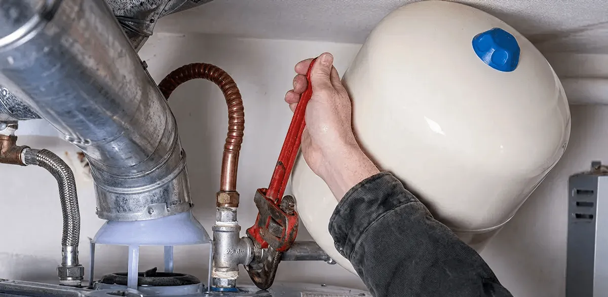 Water heater repair technician tightening plumbing connections near a tank unit in Minneapolis, MN